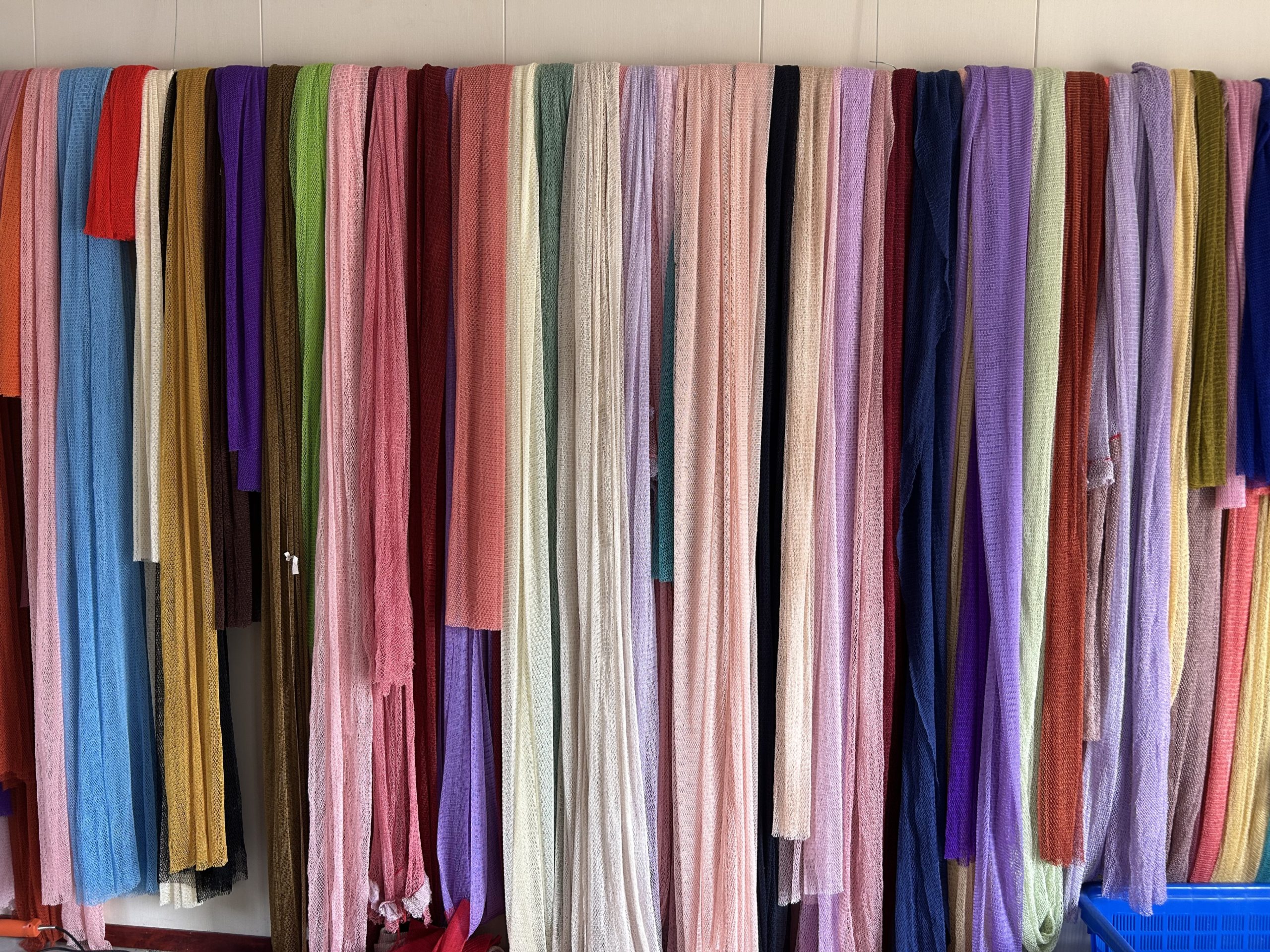 Colour range of knitted net strips hanging on a workshop rail